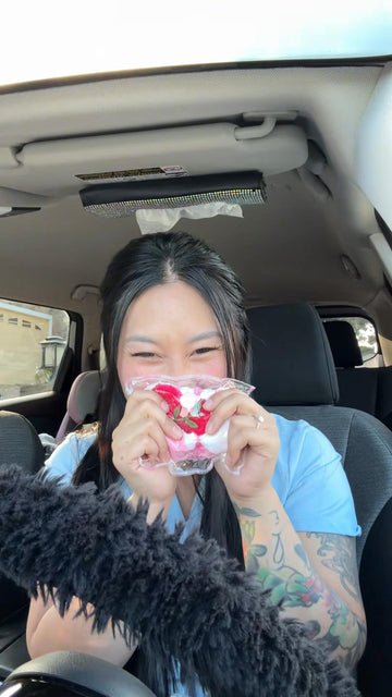 A woman smiling while holding the Creamy Tree Strawberry Rice Ball squishy toy in the car