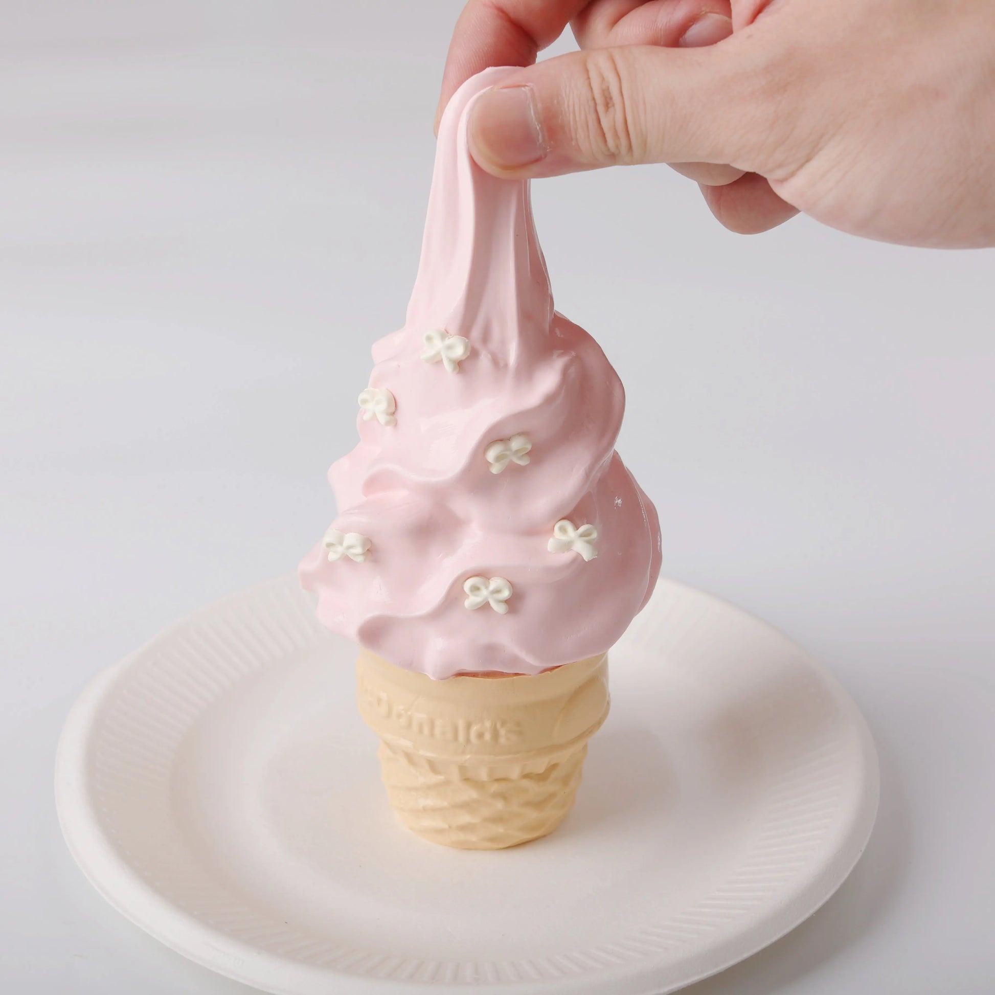 A hand squeezing Creamy Tree Strawberry Ice Cream Cone Squishy Toy