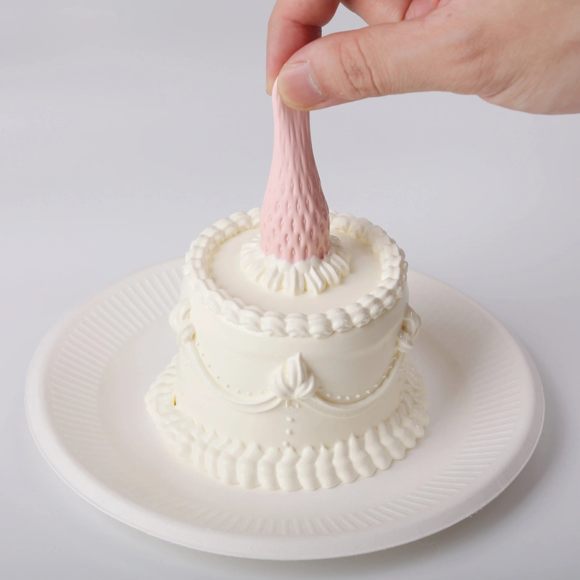 A hand is squeezing the pink strawberry on the Elodie Pink Strawberry Cake Squishy