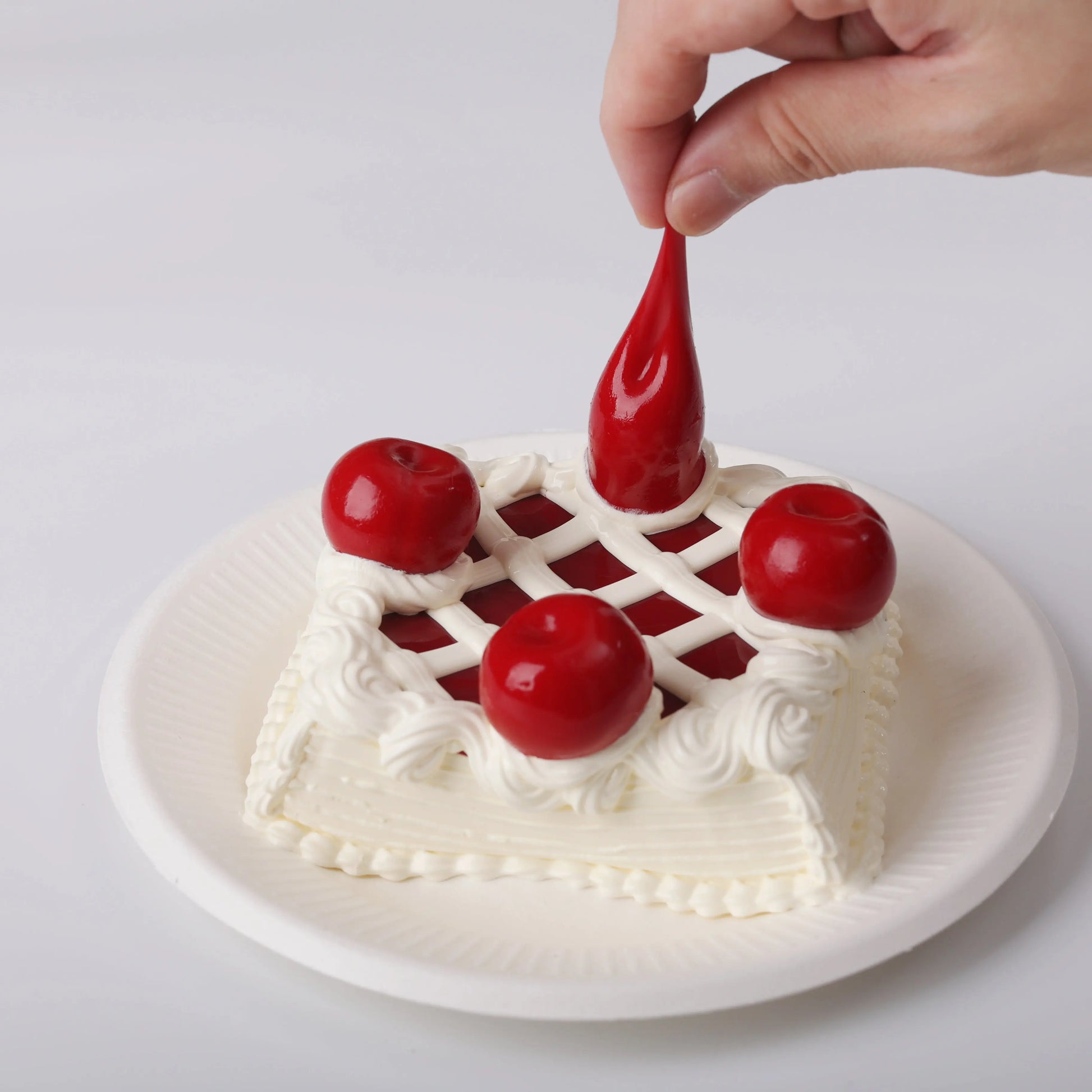 A hand is squeezing the cherry on the Sheryl Cherry Cake Squishy Toy