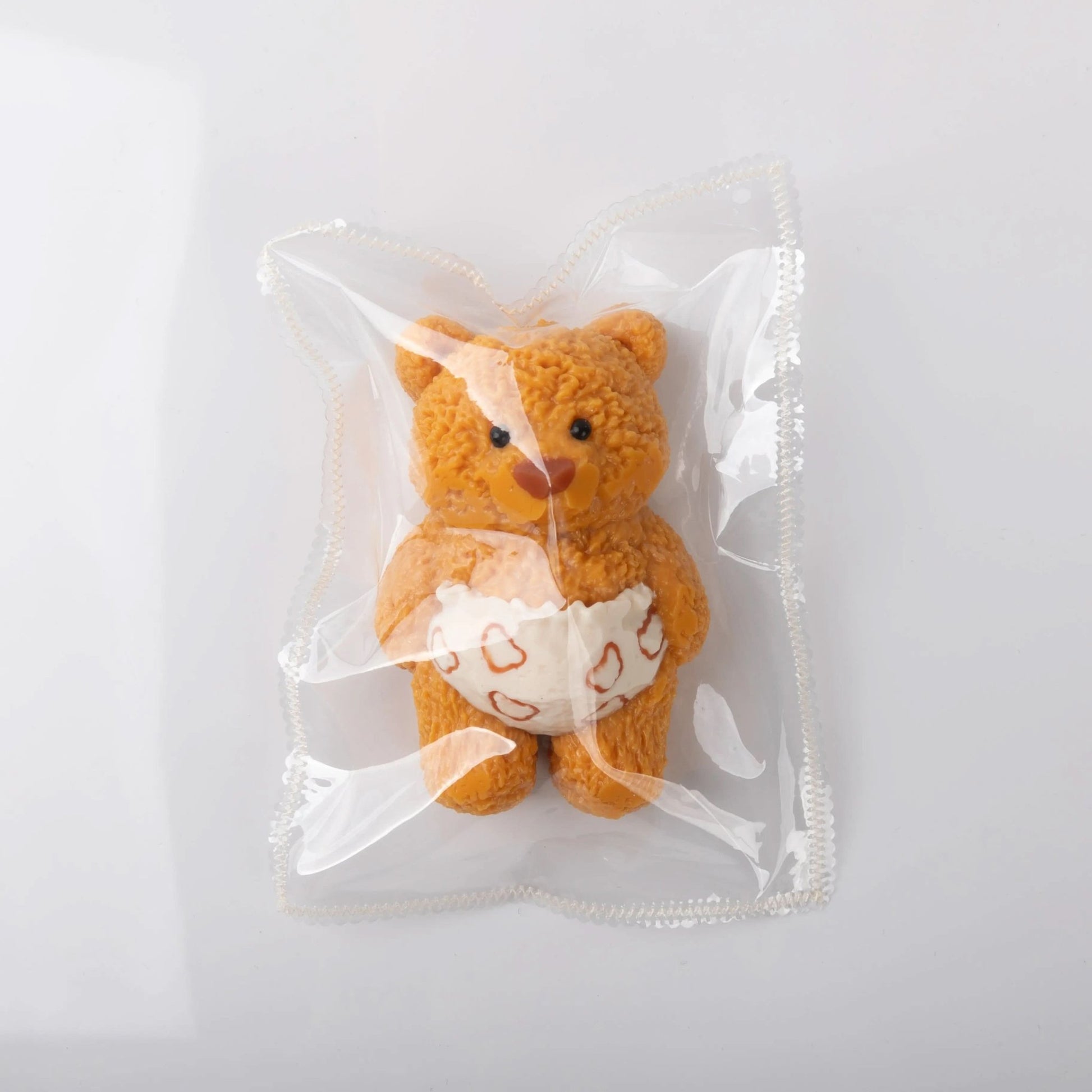 Front view of Creamy Tree teddy bear stress toy with white heart-patterned diaper in the plastic bag